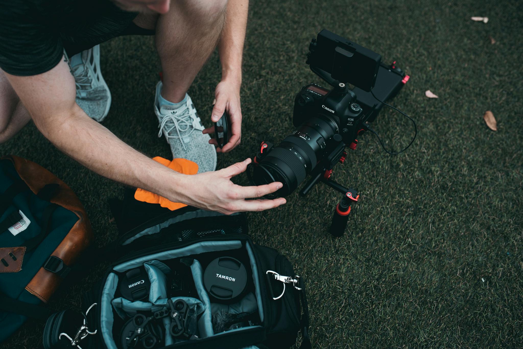 A photographer organizing camera gear and lenses on grass, preparing for a shoot.