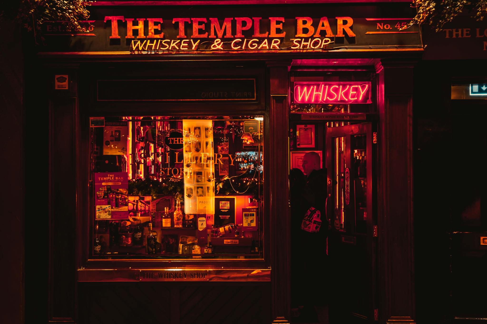 Vibrant night view of the Temple Bar, Dublin, glowing with neon lights, whiskey and cigar shop.